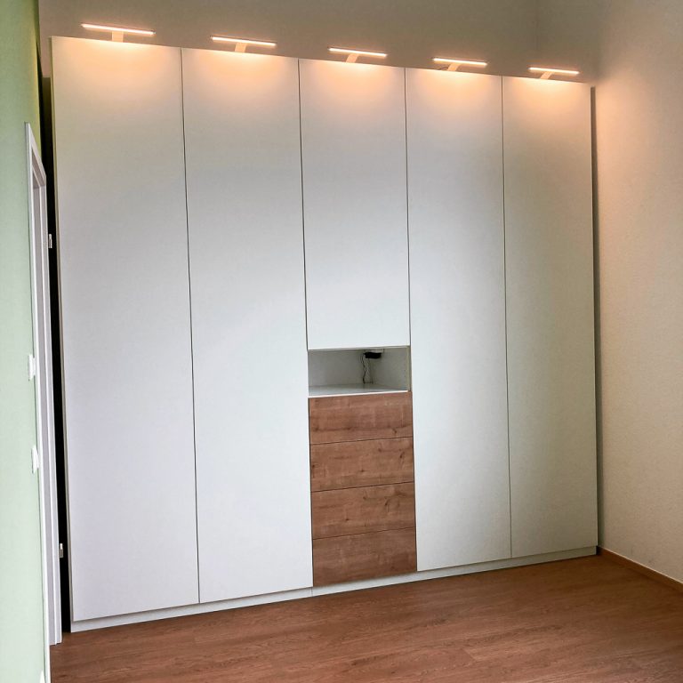 Raumhoher Einbauschrank mit weißen Türen und mittigen Holzschubladen